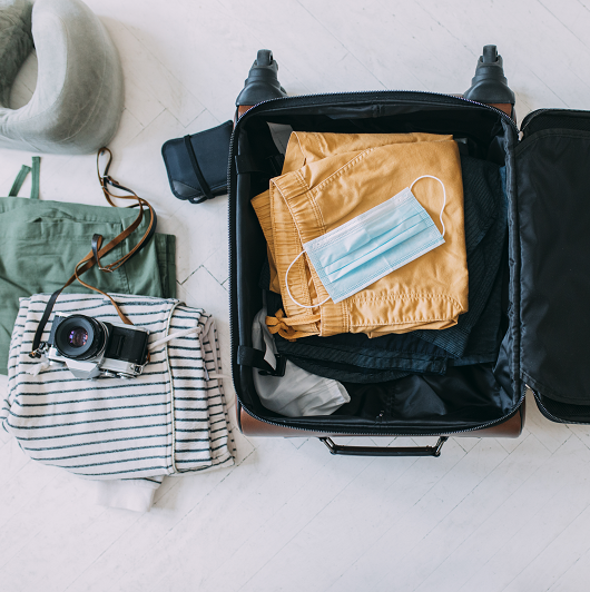 Protective face mask packed into a suitcase along with clothes and a camera. Tips for travel safety.