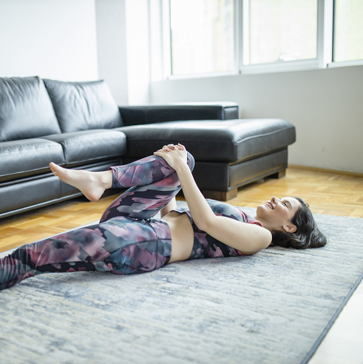 woman laying on a mat stretching pulling her knee to her chest, stretching her hip
