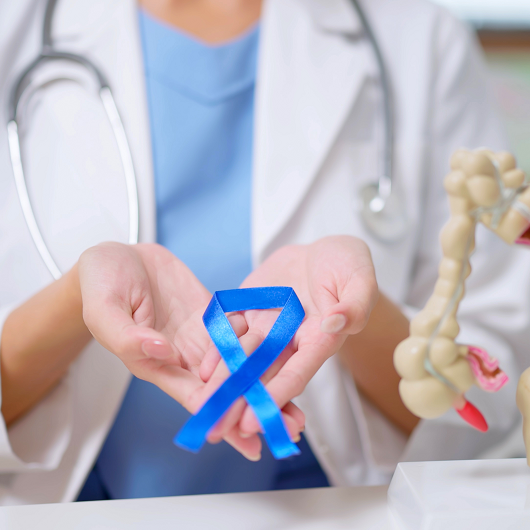 close up of female doctor hand wear white coat holds blue ribbon in front of her chest with colon model on table