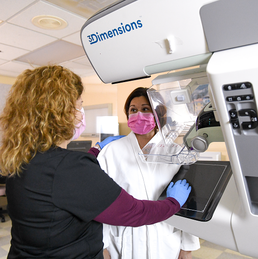 Radiologist helps a patient, in a robe, before a mammogram.