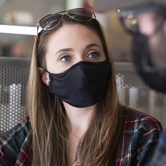 Close up shot of a woman wearing a mask, in a coffee shop, talking with someone.