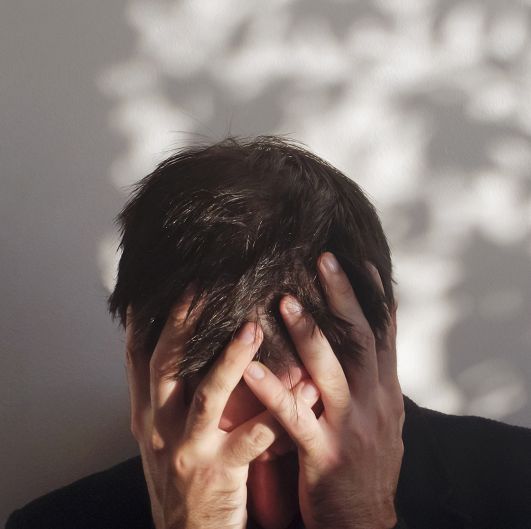 Man stressed with his hands over his face, leaning forward. Dealing with substance use disorder