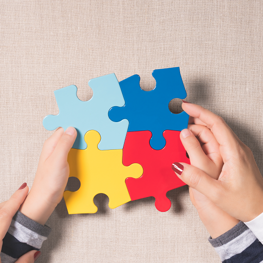 , Close-up, Top view of mother's hands holding autistic young child's hands holding colorful jigsaw puzzles (yellow, red, blue, light blue) on beige linen cloth. World autism awareness day support concept.