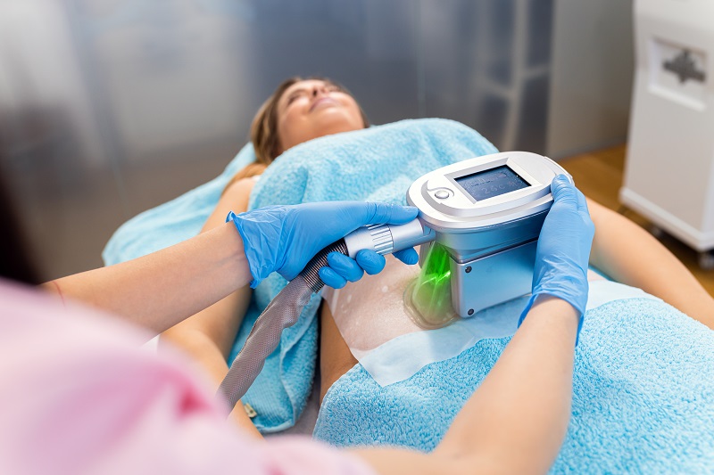 Therapist applying fat freezing cosmetic treatment, patient lying on a table. 