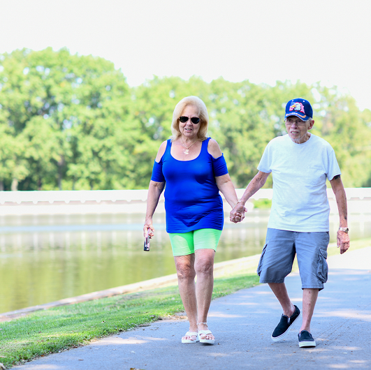 An elderly couple walking through the park together holding hands
