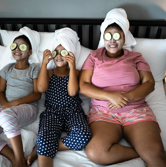 Mother and daughters in bed doing skin care with cucumber slices over the eyes