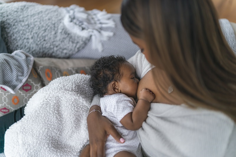 A woman breastfeeding her child on the couch at home.