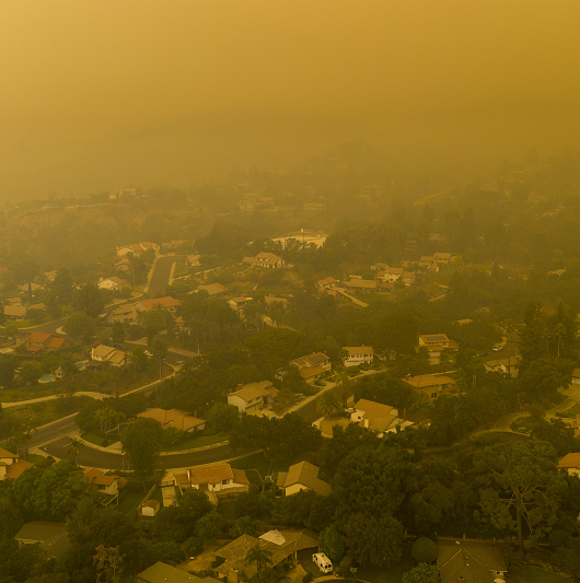 Aerial shot of a town and neighborhood covered in smoke from a fire, air pollution and hazardous air quality.