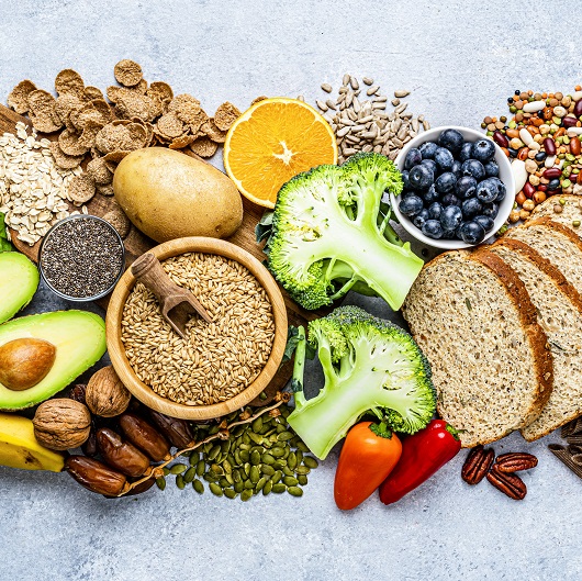 Overhead view of a large group of healthy foods like blueberries, broccoli, whole grains and nuts.