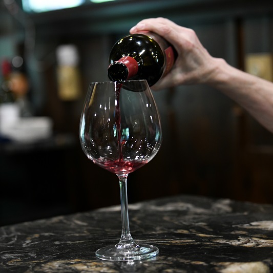 Woman's arm pouring a glass of wine at a bar.
