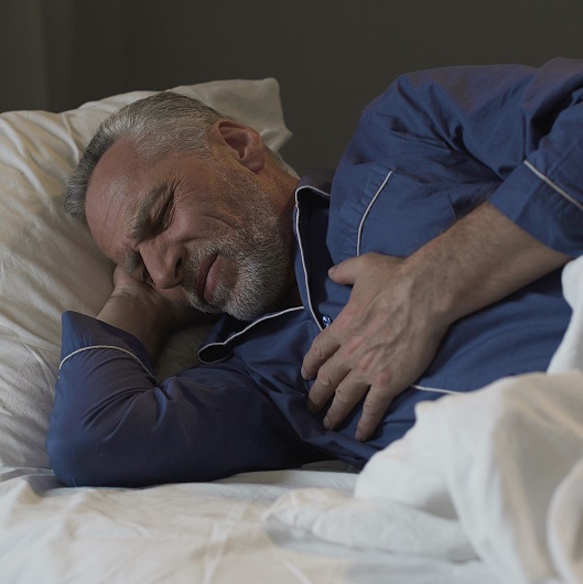 Man sleeping, suffering chest pain while laying in bed, holding his chest.
