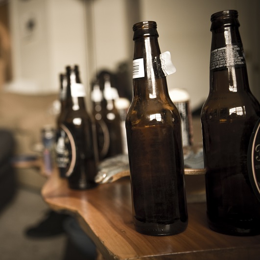 Numerous empty beer bottles on a coffee table. Binge drinking effects.