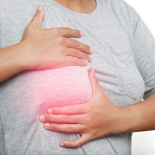 A woman in a gray shirt holding her breast feeling for a breast cancer lump.