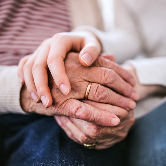 ounger caregiver holding the hands of an elderly loved one. Alzheimer's disease concept. 