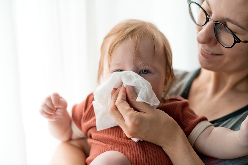 Mom helping baby clean their nose with a tissue.