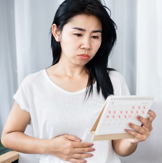 Woman holding a calendar, hand on her stomach, worried about missing her period.