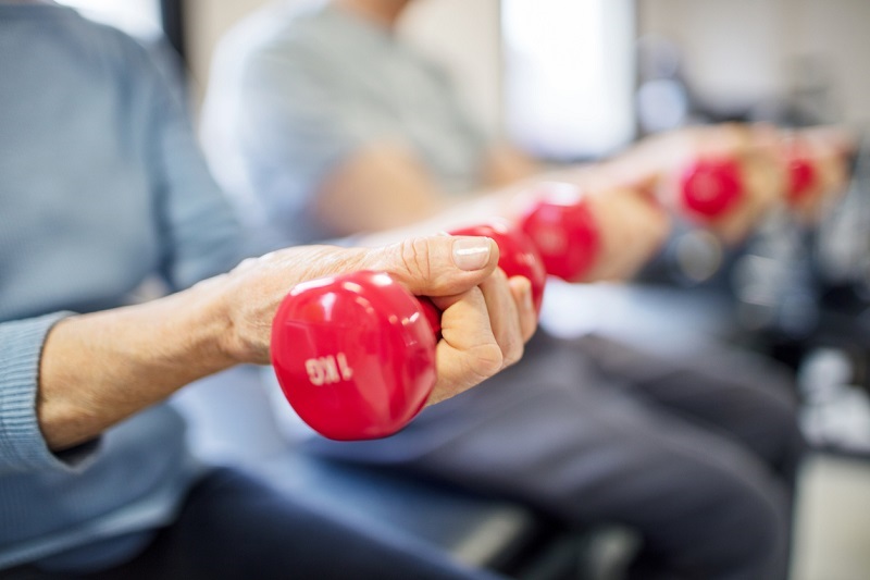 Midsection of senior woman lifting dumbbells for strength training.