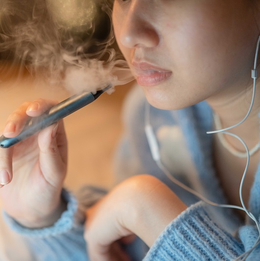Close up shot of a young woman vaping an electronic cigarette at night