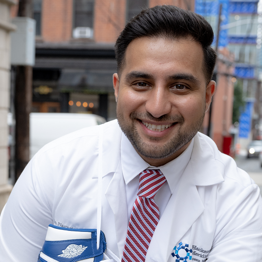 Zain Nagaria, M.D. smiling, with a pair of sneakers over his shoulder, in Hoboken NJ