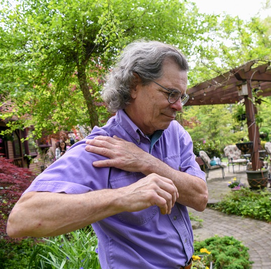Man outside, holding his shoulder in pain while lifting his arm up.