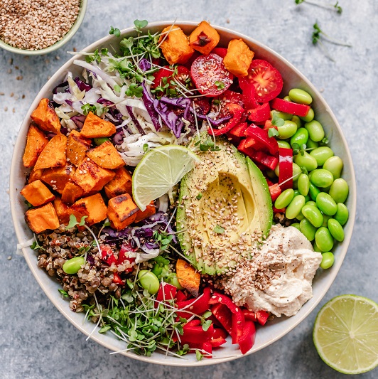 Overhead view of a colourful vegan bowl with quinoa, sweet potato, avocado, hummus and variety of veggies
