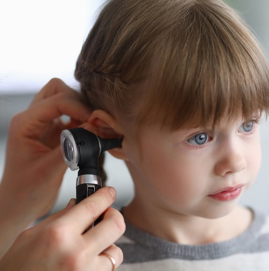 Otorhinolaryngologist examines a little girl's ear with an otoscope.