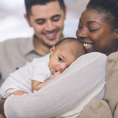 New mom holds her baby to her chest, with dad sitting close by on the couch.