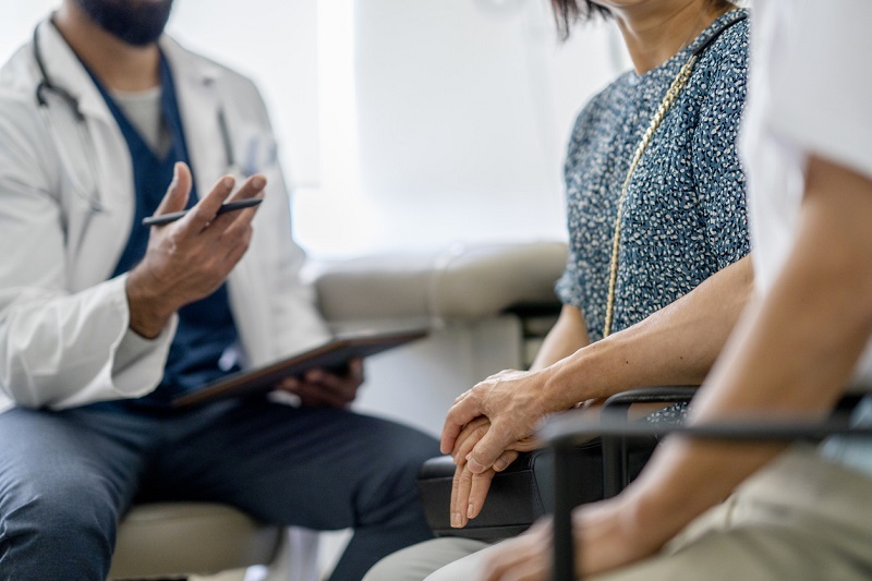In a patient room - the doctor is explaining something to the patient and a loved one, who are holding hands.