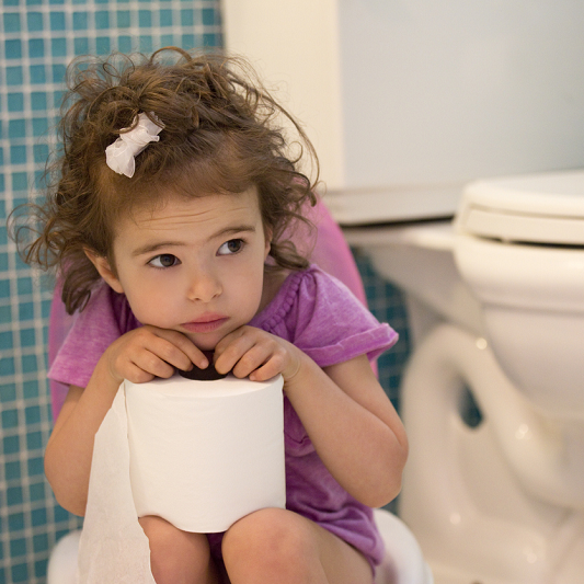 Little girl sitting on the potty in the bathroom, holding a roll of toilet paper.