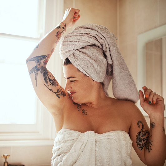 Woman in a towel, smelling her armpit, observing body odor.