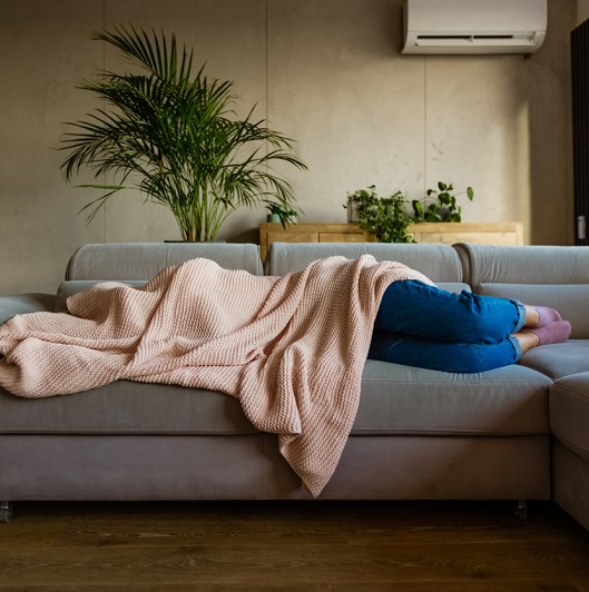 Young woman lying down on sofa in living room covered by blanket.