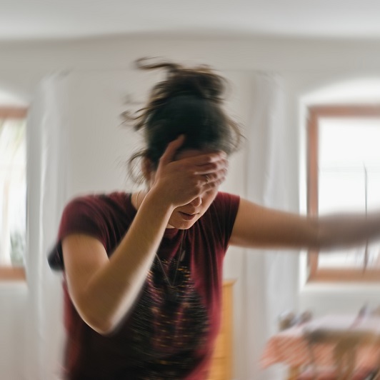 Woman standing, one hand on her forehead, one on the wall, trying to regain balance. Suffering from vertigo.