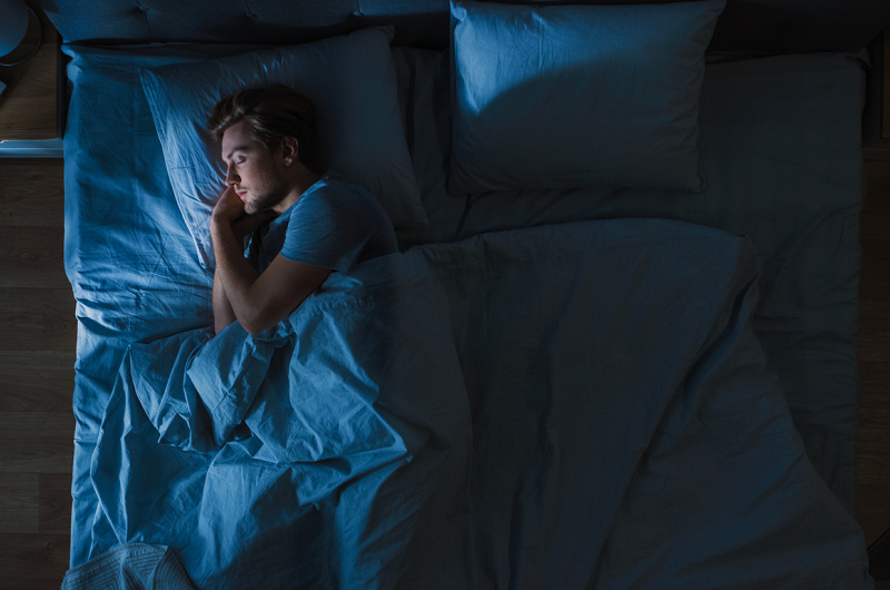 Man sleeping in a dark room in his bed.