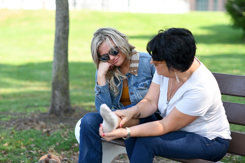 Mother and daughter sitting on bench, mother is looking at daughter's foot assessing injury.