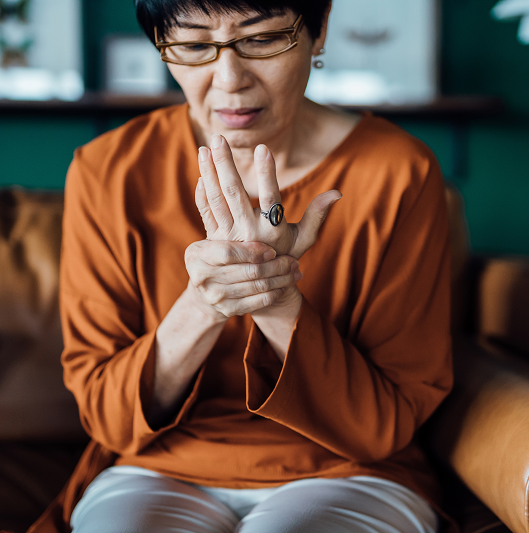 Woman rubbing her hands in discomfort, suffering from arthritis in her hand while sitting on the sofa at home.