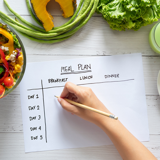 Overhead view of someone meal planning for the week, with healthy foods on the table.