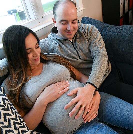 Husband and pregnant wife sitting on the couch smiling and feeling the baby move, with hands on her belly. 