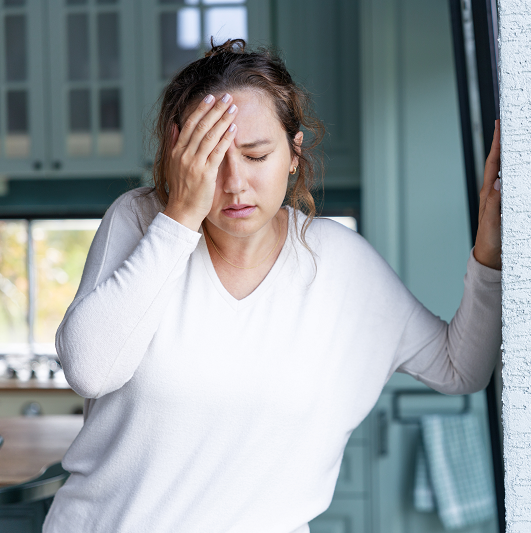Woman with one hand on her forehead, the other resting on a wall for balance. Experiencing dizziness.