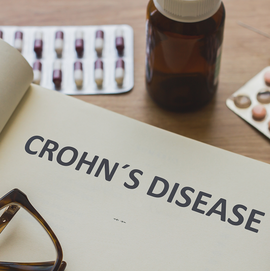 A book opened that says "Crohn's Disease" on the cover page. Around the book are reading glasses and some medications.