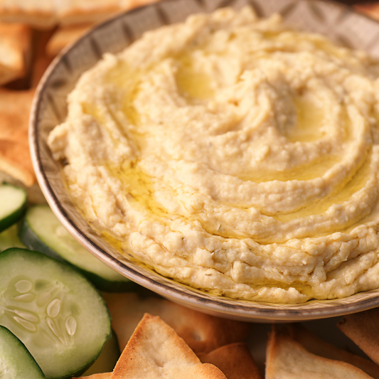 Lemon, garlic and white bean hummus in a bowl with sliced cucumbers and pita surrounding it.