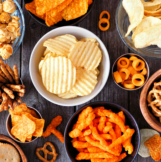 An assortment of chips and processed snacks in bowls on a table.