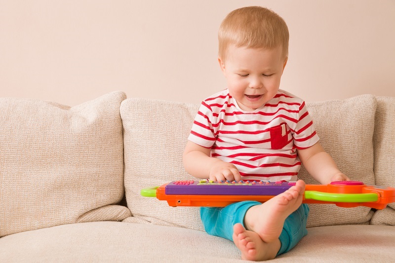 Toddler playing an electric piano toy on the couch.