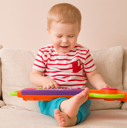 Toddler playing an electric piano toy on the couch.