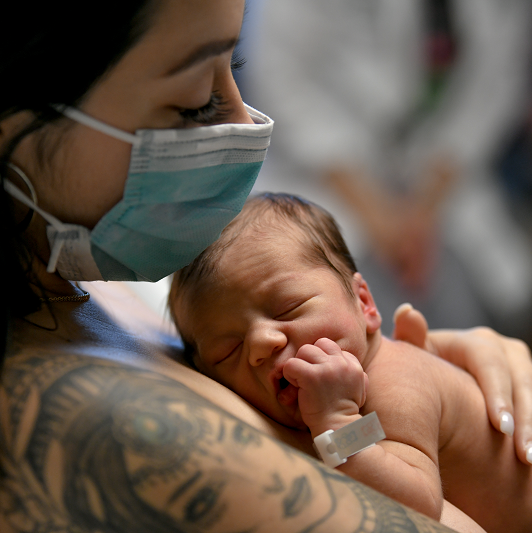 Mom holds newborn baby to chest for skin to skin contact. Image concept for c-section recovery.