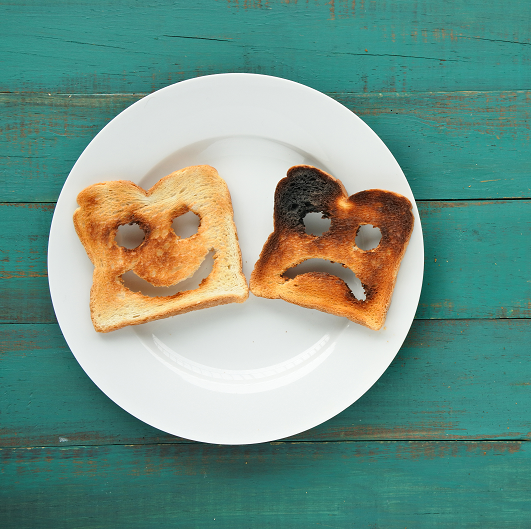 Flat lay view of two slices of toasted bread on a white plate; one has a happy face, and the other is sad.