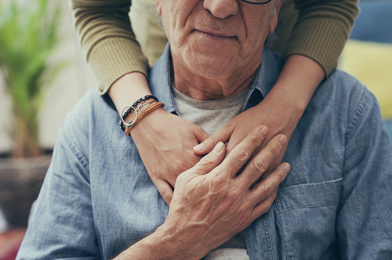 Woman's hand on a man's shoulder offering comfort.