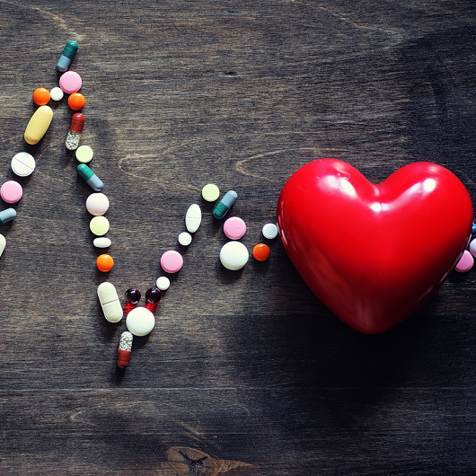 Heart supplement pills on a wooden countertop, with a red heart.