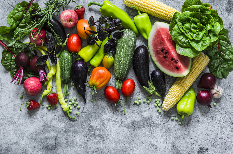 Fresh garden organic vegetables, berries, and fruits on a gray background, top view.