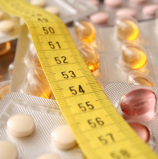 Measuring tape over weight loss pills on a table.
