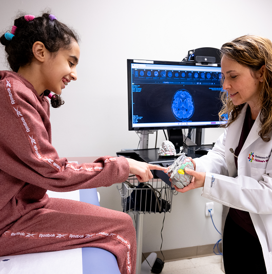 Pediatric neurologist Felicia Gliksman, D.O., and a patient looking at an anatomical model of a brain.